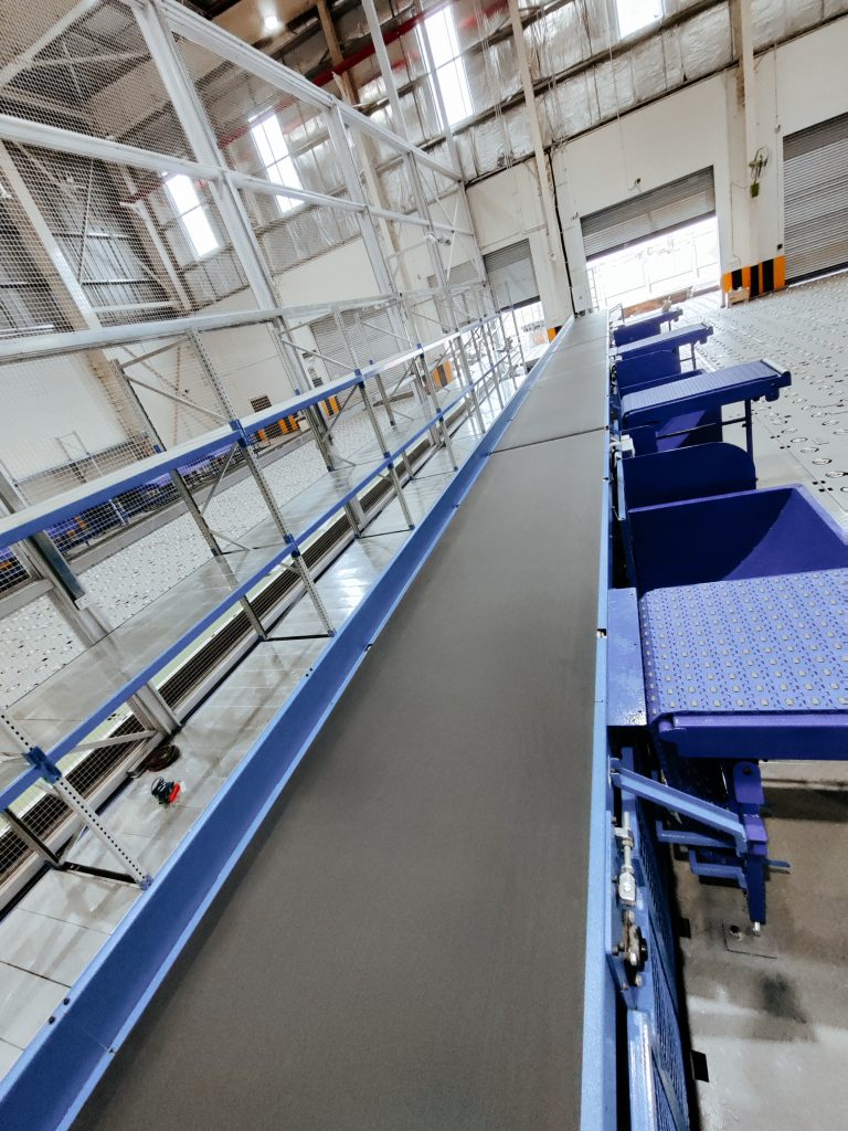 Horizontal belt conveyor system inside an industrial warehouse for automated material handling and product transportation.