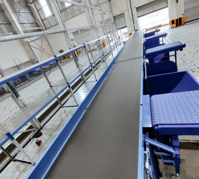 Horizontal belt conveyor system inside an industrial warehouse for automated material handling and product transportation.